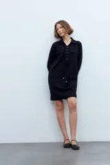 Vestido corto negro con cuello camisero, mangas largas, cierre frontal con cordones y bolsillos de parche en el pecho y las caderas.