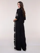 Conjunto de dos piezas negro compuesto por camisa de manga corta con cuello camisero y pantalón palazzo de tiro alto. Presenta detalles de bordados florales en contraste a lo largo de los laterales del pantalón y en las mangas.