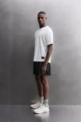 Camiseta de ajuste relajado (relaxed fit) color terracota, confeccionada en tejido técnico. Presenta cuello redondo, mangas ranglán cortas y un parche negro con logo en el bajo.