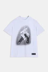 Buzo blanco de manga corta, corte oversize, con cuello redondo. Presenta un estampado frontal en blanco y negro de una persona con gafas de sol en pose agachada, con un efecto de halo o relámpagos alrededor. Incluye una etiqueta negra con logos en la parte inferior derecha.