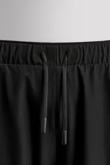 Pantalón de jogging negro confeccionado en tejido técnico ligero y elástico, corte slim fit, con cintura elástica ajustable con cordón, bolsillos laterales y trasero con cierre de cremallera, bandas reflectantes en las piernas y bajos ajustables con cremallera.