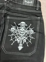 Jean negro de corte regular fit, con bolsillos traseros amplios que cuentan con un estampado gráfico en color blanco de calaveras y diseño gótico.