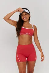 Conjunto deportivo compuesto por un top y un short de tiro alto en color bordó con detalles de líneas blancas. El top presenta breteles anchos y el logo de la marca en el frente, mientras que el short tiene un diseño ajustado con costuras laterales visibles.