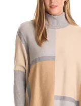Polera tipo poncho de corte oversize, con cuello alto tejido y mangas largas con puños elásticos. Presenta un diseño geométrico de bloques de color en tonos beige, gris y tostado.