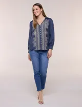 Camisa de estilo boho, color verde, con cuello camisero, escote en V y botonadura frontal con botones perlados. Cuenta con una pechera con bordados geométricos y florales a contraste, mangas largas abullonadas con puños abotonados y delicados bordados dispersos.