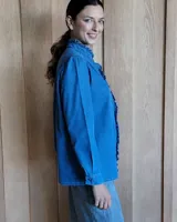 Camisa de jean azul con cuello alto con volados y volados en el frente.