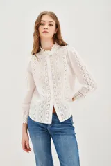 Camisa de algodón blanca con cuello alto tipo victoriano, cierre frontal con botones y detalles de encaje vertical a lo largo del frente y las mangas. Presenta mangas largas con puños de encaje y un diseño romántico y delicado.