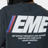 Remera oversized color gris oscuro, con estampado frontal y trasero del logo "EME" en blanco con detalles en azul y rojo, y texto adicional en blanco. Confeccionada en 100% algodón y con corte cropped.