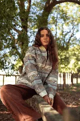 Campera de jean con cierre frontal y cuello tipo bomber, presenta un estampado horizontal con motivos paisajísticos y geométricos en tonos azules, marrones y beige. Posee puños de tela elástica en color blanco.