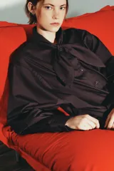 Camisa de manga larga en tejido de popelín color bordó, con cuello tipo pañuelo con nudo frontal, cierre de botones y puños con pliegues.