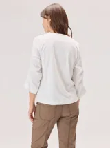 Remera de algodón color blanco, con cuello redondo y mangas tres cuartos con volados escalonados y detalles de pespuntes.
