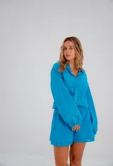 Conjunto de dos piezas compuesto por una camisa de corte relajado con mangas abullonadas, puños elásticos y cierre frontal de botones, y un short de tiro medio con cintura elástica. Ambas prendas están confeccionadas en lino liviano de color turquesa.
