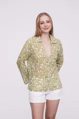 Blusa de algodón con estampado de hojas en tonos verdes sobre fondo blanco, cuello camisero, cierre frontal con botones y mangas largas.