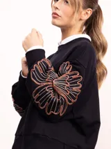 Buzo de algodón color negro con cuello redondo, mangas largas y bordado floral XL en color cobre en las mangas. Presenta un diseño holgado y cómodo.