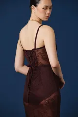Vestido midi de encaje color marrón chocolate, con diseño tipo corset en el torso y breteles finos. Presenta transparencias en la falda y detalles de encaje en el escote.