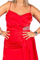 Vestido largo de fiesta color rojo, confeccionado en satén brillante, con breteles finos, escote cruzado, tajo en la pierna y detalle de aplique de pedrería en la cintura.