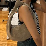 Cartera tipo hobo de gamuza color beige con asa anudada al hombro y logo grabado en la parte inferior.