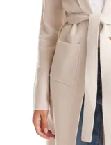 Chaqueta de punto color beige con frente abierto, cuello con solapa, mangas largas y bolsillos frontales. Incluye un lazo para ajustar en la cintura.