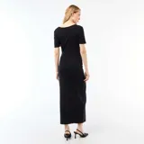 Vestido largo negro de manga corta y cuello redondo, con diseño ajustado y detalle drapeado en la cintura adornado con un aplique metálico dorado.