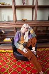 Sweater de lana merino tejido artesanalmente, con diseño pintado a mano que combina tonos violeta, verde y naranja. Presenta cuello redondo, mangas largas y un corte holgado y cómodo.
