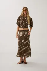 Blusa marrón con estampado de lunares en tonos claros, escote redondo y frunce frontal con cordón ajustable. Cuenta con mangas cortas abullonadas y diseño corto.