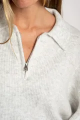 Sweater de punto en color gris melange, con diseño oversize, cuello polo y cierre frontal parcial. Presenta mangas largas y una textura acanalada suave.
