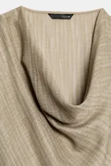 Camisa de cuello fluido y manga larga con puños anchos, de corte recto y largo medio, confeccionada en tejido rústico en tono beige con sutil textura jaspeada. Cuenta con un cinturón ajustable del mismo género para entallar la cintura.