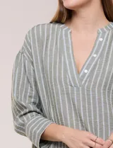 Blusa de silueta holgada a rayas verdes y blancas, confeccionada en tela liviana con textura arrugada. Presenta cuello en V profundo con botones frontales, mangas 3/4 de hombro caído y ruedo asimétrico con aberturas laterales.