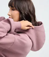 Buzo femenino de corte holgado, color malva, con capucha, manga larga con puños elásticos y bolsillo tipo canguro frontal.