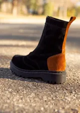 Borcego de cuero con diseño bicolor, combinando cuerpo en color negro y detalle en talón y lengüeta trasera en color suela. Cuenta con suela track cosida y cierre lateral.