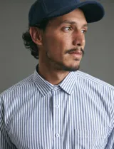 Camisa de manga larga con estampado de rayas verticales en azul y blanco, cuello clásico y bolsillo frontal.