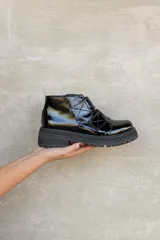 Borcego de cuero charolado negro con suela track dentada y cierre mediante tiras con velcro.