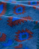 Buzo de polar fleece con diseño estampado geométrico en tonos azules, bordó y verde. Presenta cuello alto con cierre de botones a presión, bolsillo frontal con solapa en contraste y puños elásticos.