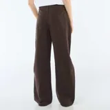 Pantalón de jean color marrón con corte globo, tiro alto y diseño de pierna ancha. Presenta costuras laterales marcadas y cierre frontal con botón y cremallera.