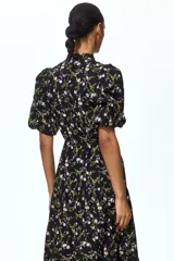 Vestido largo negro con estampado floreado, cuello mao, mangas globo cortas y falda escalonada con volados.