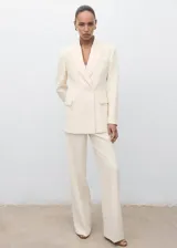 Chaqueta de traje color beige, con cuello de solapa, cierre cruzado con un botón y bolsillos con solapa en los laterales y en el pecho.