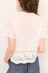 Camisa azul de manga corta confeccionada en tejido broderie con diseño calado y floral. Cuenta con escote en V y cierre frontal de botones.