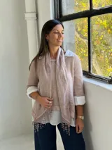 Sweater de punto rosa claro con diseño de capas, que incluye una camisa blanca debajo y un pañuelo a juego con detalles de encaje y flecos en el ruedo.