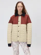 Campera acolchada de diseño colorblock, con el pecho y hombros en tono bordó y el cuerpo y mangas en color beige. Presenta cuello camisero y puños de pana negra, cierre frontal oculto con botones a presión y costuras pespuntadas en patrón cuadriculado.