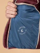 Chaleco acolchado de hombre color gris, con diseño matelasseado horizontal, cuello alto y cierre frontal completo. Presenta un calce ajustado y detalle de logo circular bordado en el pecho.