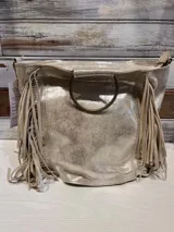 Cartera de cuero color dorado con acabado metalizado, diseño con flecos laterales y manija circular metálica.
