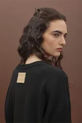 Sweater de punto color negro, de corte holgado y manga larga, con detalle de bordado calado en los hombros y a lo largo de las mangas.