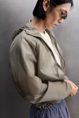 Chaqueta cortavientos de tejido técnico con estructura ripstop, cuello subido con capucha, cierre frontal de cremallera, bolsillos laterales ocultos y zonas perforadas para mayor transpirabilidad.
