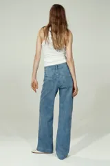 Jean de denim de algodón con leve stretch, tiro alto y piernas amplias de corte holgado. Presenta bolsillos traseros de parche, cierre con botón y pliegues en la parte delantera y trasera.