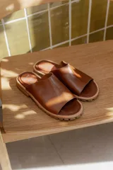 Sandalias tipo chinelas de cuero color marrón, con diseño de banda ancha sobre el empeine y suela track dentada.