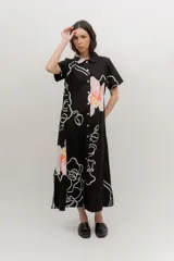 Vestido midi de popelina de algodón negra, con estampado floral en tonos rosados y blancos, cuello tipo bebe, mangas cortas, cierre frontal abotonado y bolsillos laterales.