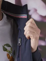 Campera azul marino con cierre frontal, cuello alto y bolsillos laterales con cierre. Tiene un parche rojo con cierre en la manga izquierda y un diseño acolchado en la parte delantera.