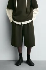 Bermuda de corte oversized confeccionada en tejido técnico compacto con elasticidad. Presenta cintura elástica ajustable con cordón, pinzas en el delantero y la espalda, y bolsillos laterales.