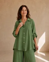 Camisa de lino verde oliva, de corte oversize y largo asimétrico, con cuello camisero, cierre frontal de botones, bolsillo aplicado en el pecho y mangas largas regulables con presilla.