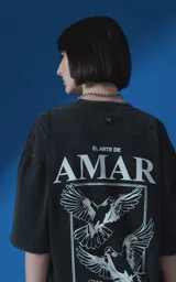Remera de manga corta con cuello redondo y calce oversize, confeccionada en algodón premium con efecto de lavado nevado. Presenta una estampa gráfica en la espalda con diseño de palomas y texto alusivo.
